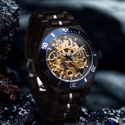 A luxury wood skeleton watch with a dark metallic case and band, featuring a blue bezel and a highly visible gold-toned mechanical movement through the dial, set against a dark, moody background.