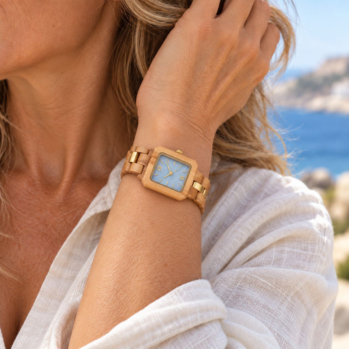 Woman in white linen wearing The Blue Pearl slim wood watch by the sea